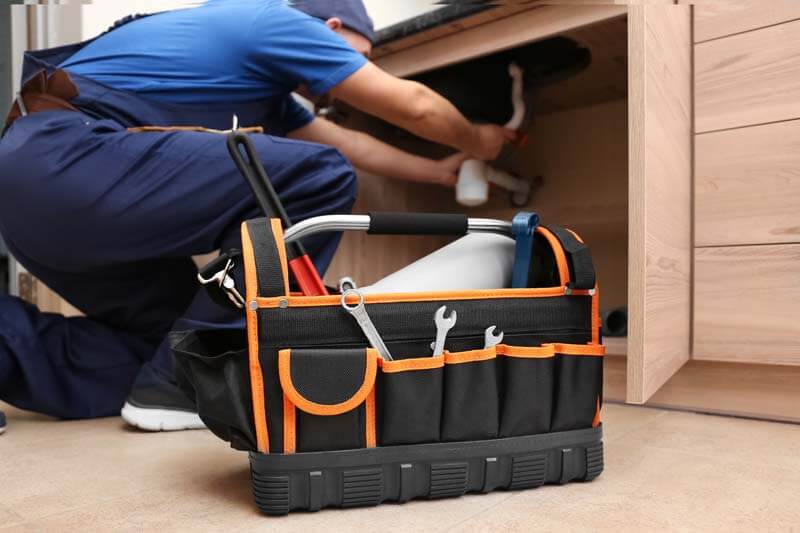 Plumber With Set Of Tools Repairing Sink In Kitchen